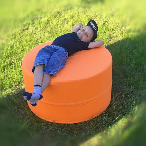 Dziecko odpoczywające na pomarańczowej okrągłej pufie na trawie
